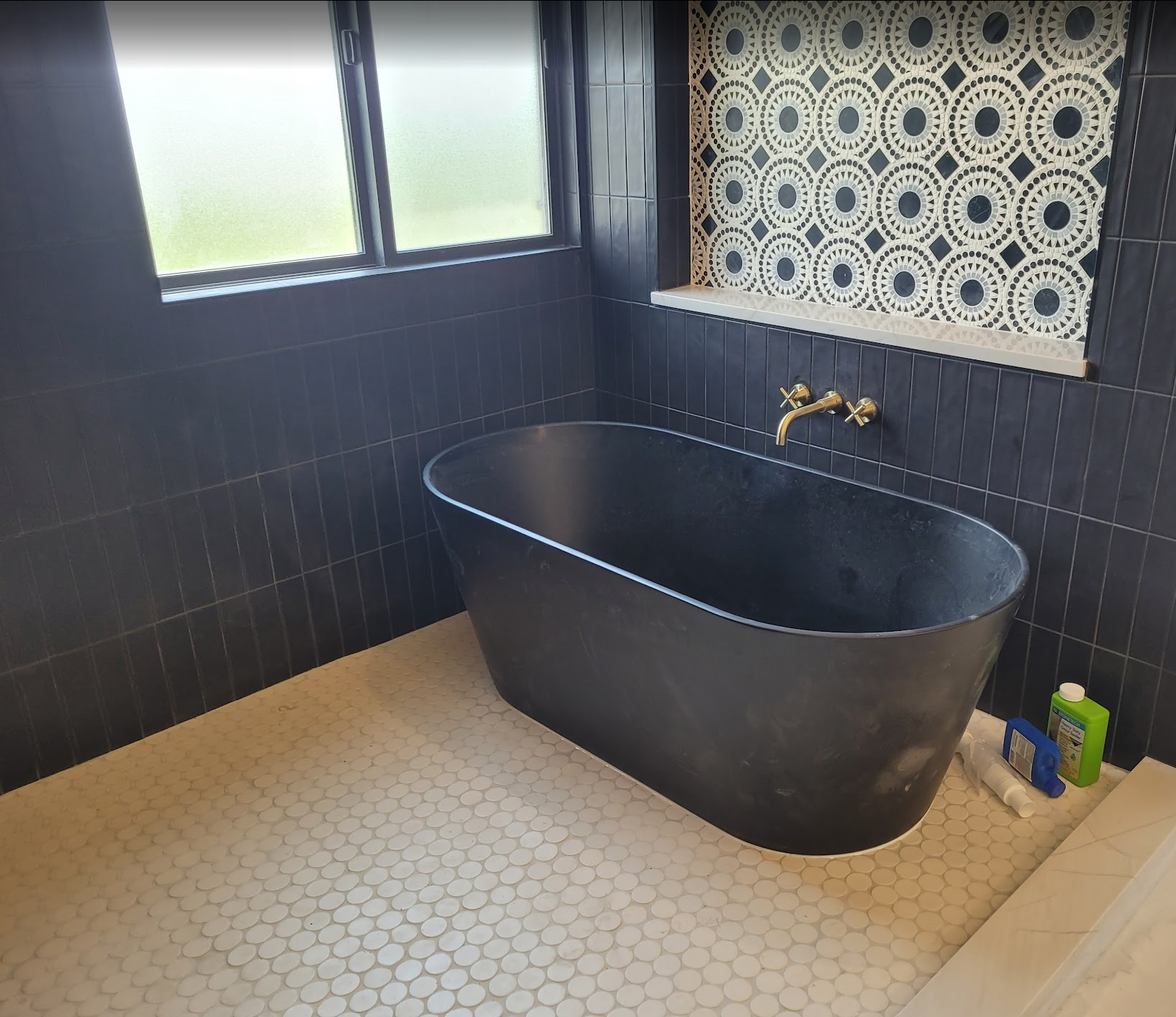 Black freestanding tub against navy vertical tile with brass fixtures